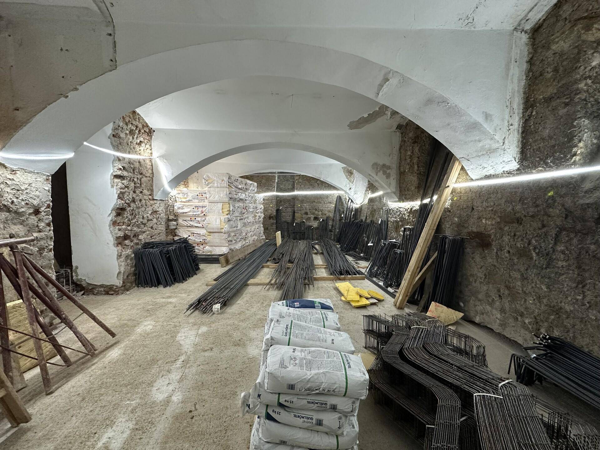 Historischer Kellerraum im Rohbau mit Gewölbedecken, unverputzten Wänden und Baumaterialien.