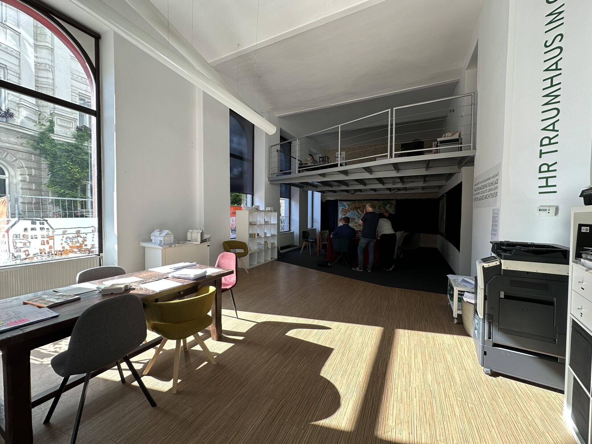 Geräumiger Verkaufsraum mit Holzboden, hohen Fenstern und einer sichtbaren Galerie im Hintergrund.