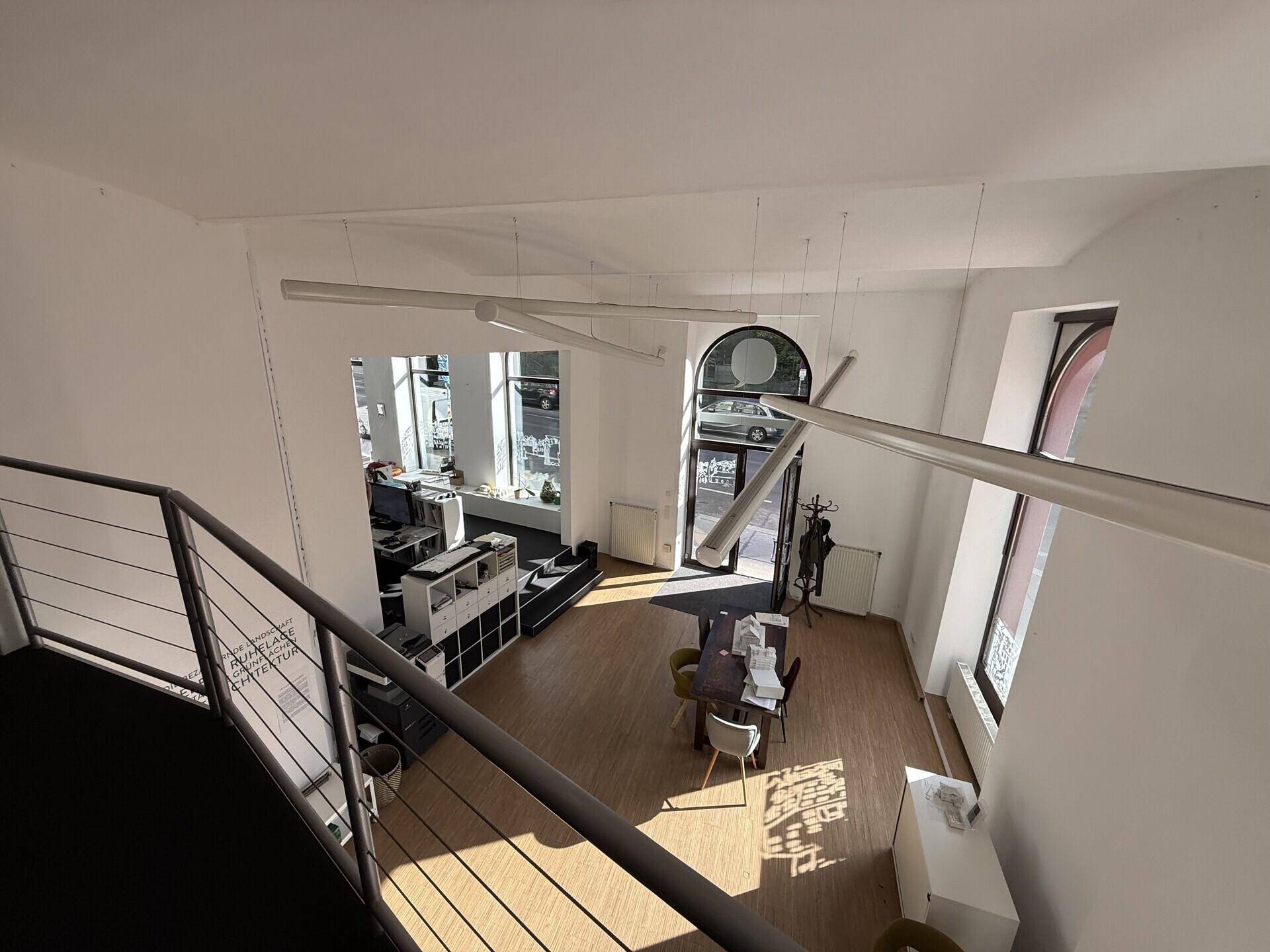 Blick von der Galerie auf den offenen Verkaufsraum mit hohen Fenstern und modernen Hängelampen.