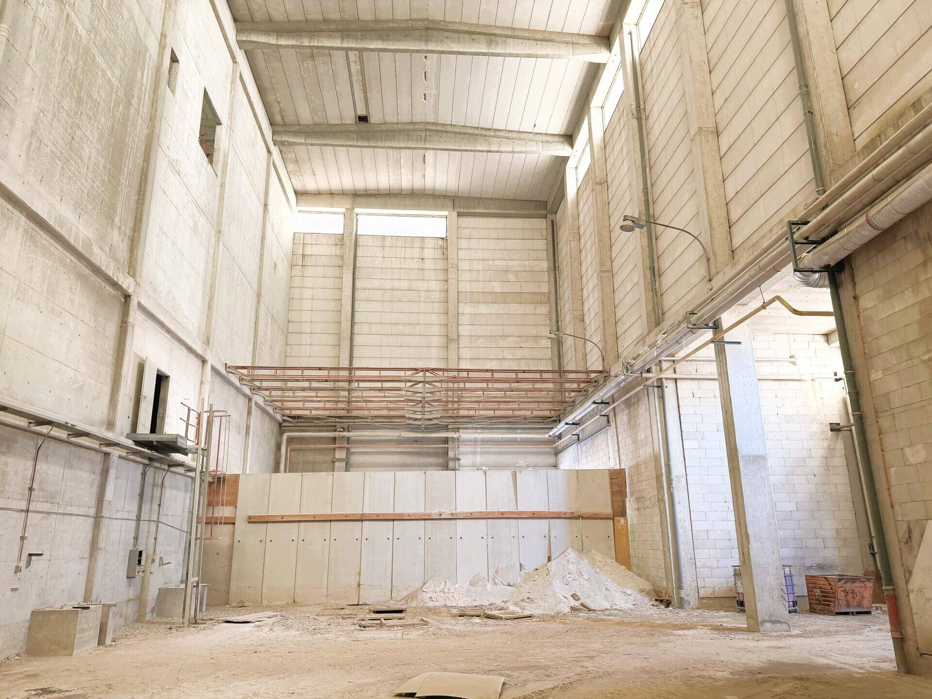 Hohe Lagerhalle mit Betonwänden, sichtbaren Trägern und viel vertikalem Raum für Lagerung.