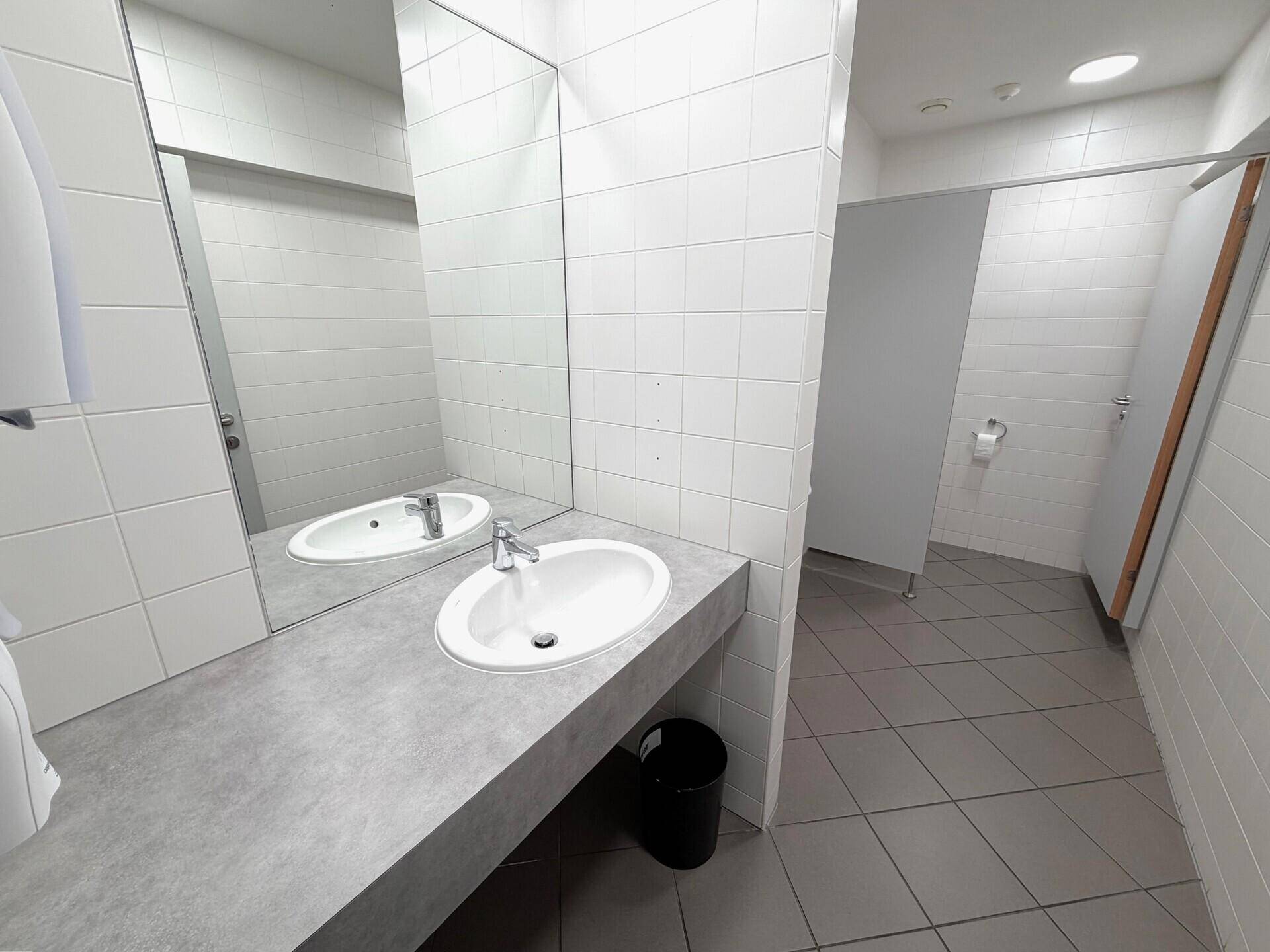 Heller Sanitärbereich mit mehreren Waschbecken, großen Spiegeln und gefliesten Wänden.