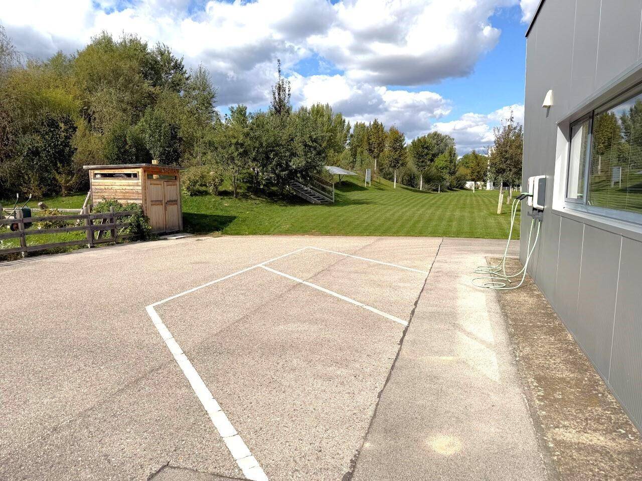 Außenparkplatz mit markierten Stellflächen und Ladestationen für Elektrofahrzeuge am Gebäude.