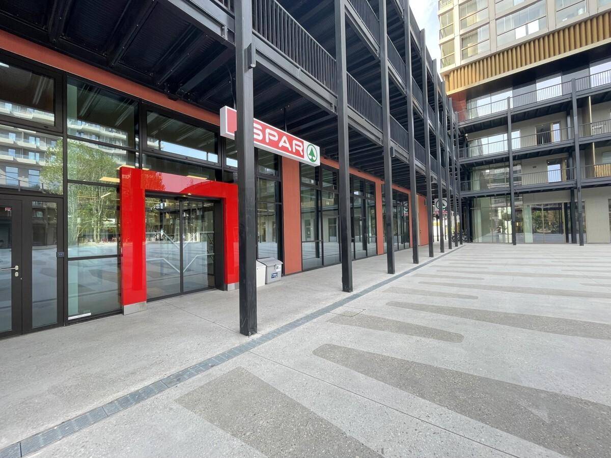 Nahaufnahme des Erdgeschosses eines modernen Gebäudes mit großen Schaufenstern und einem Supermarkt-Eingang.