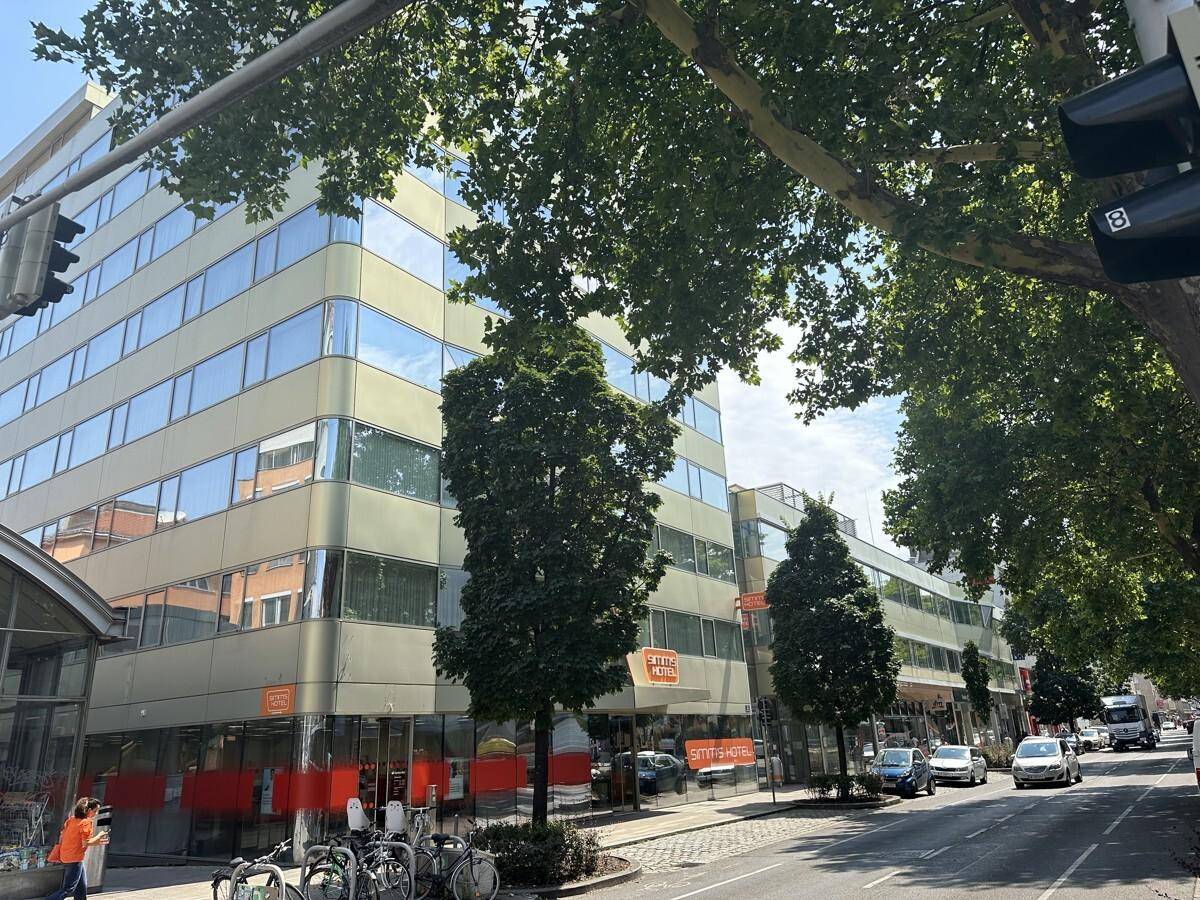 Ansicht eines modernen Bürogebäudes mit reflektierenden Fenstern und Geschäften im Erdgeschoss an einer städtischen Straße.