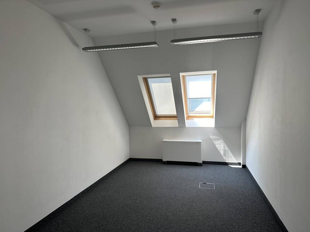 Kompakter Büroraum im Dachgeschoss mit Teppichboden, schrägen Wänden und zwei Dachfenstern.