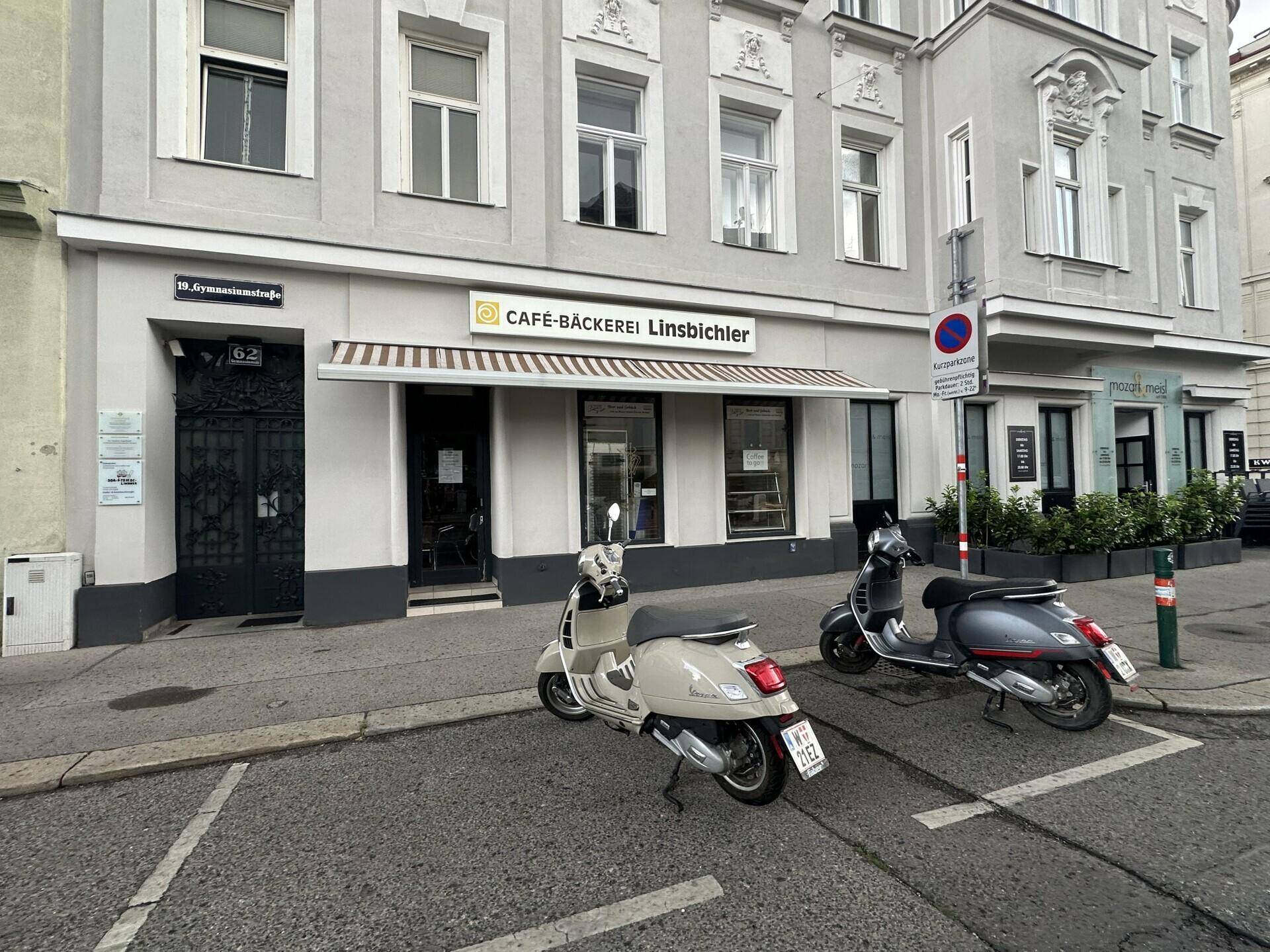 Historische Gebäudefassade mit Café-Bäckerei im Erdgeschoss und geparkten Rollern davor.