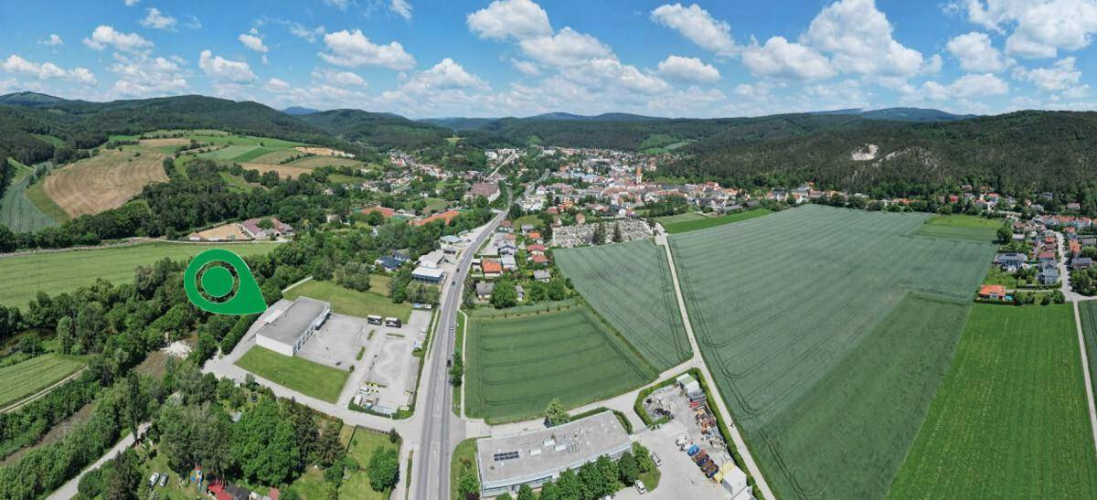 Panoramablick aus der Vogelperspektive auf eine ländliche Stadt, umgeben von Feldern und bewaldeten Hügeln.