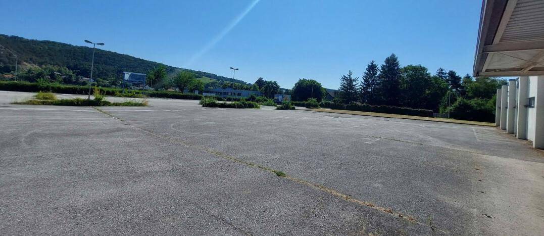 Weitläufiger asphaltierter Parkplatz unter blauem Himmel mit bewaldeten Hügeln im Hintergrund.