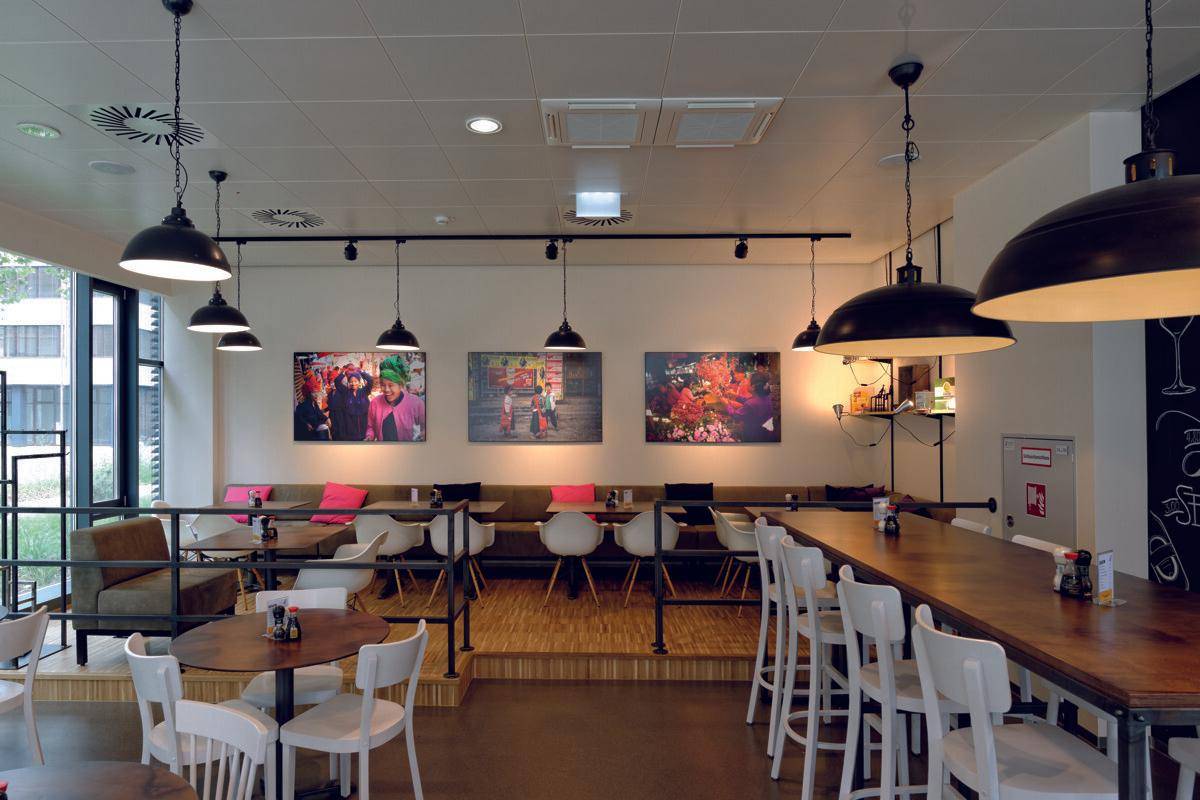 Geräumiges Restaurant mit verschiedenen Sitzbereichen, Barhockern und farbenfrohen Wandbildern.