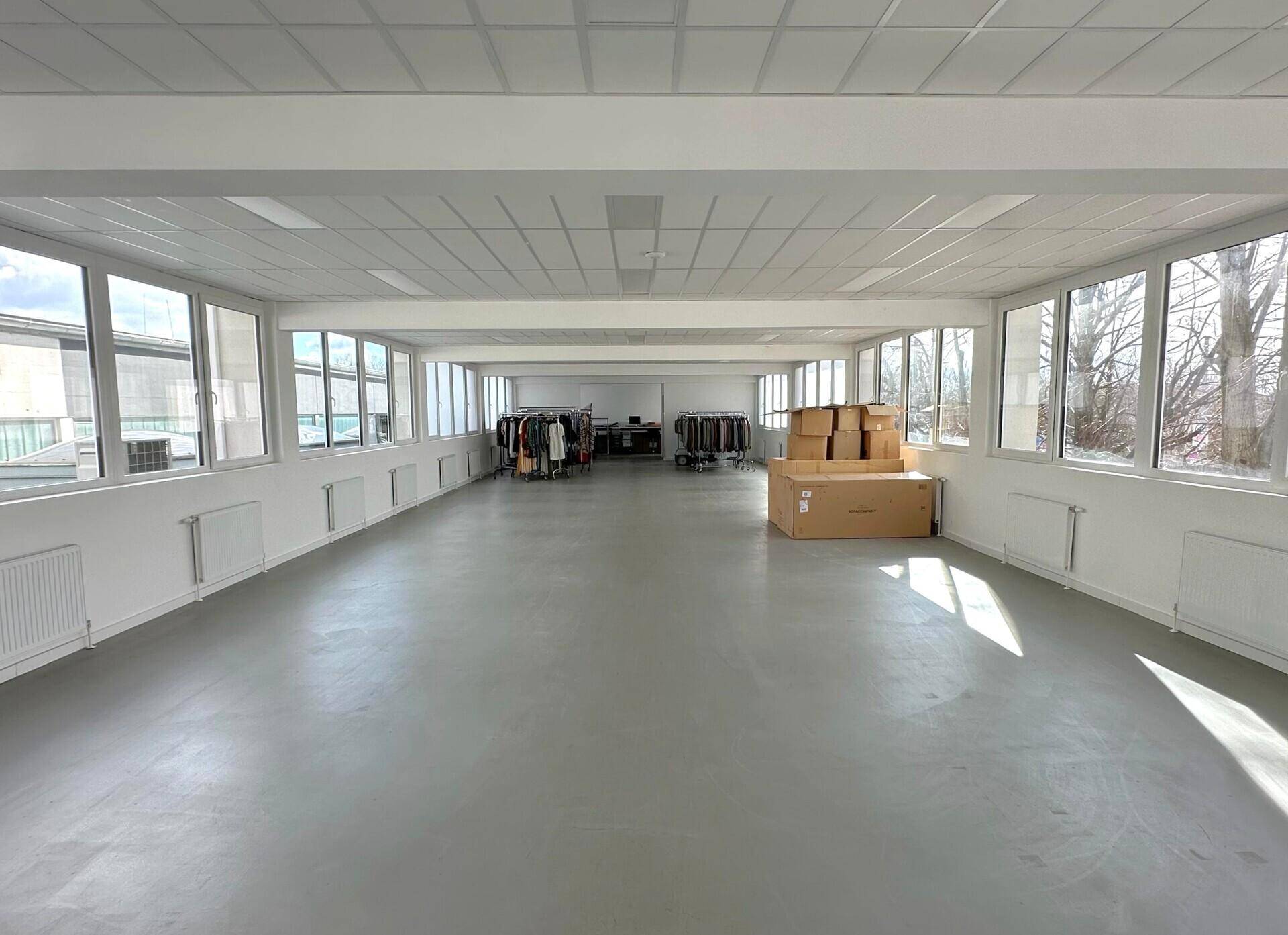 Großer, heller Gewerberaum mit vielen Fenstern, hohen Decken und einem modernen Betonboden.