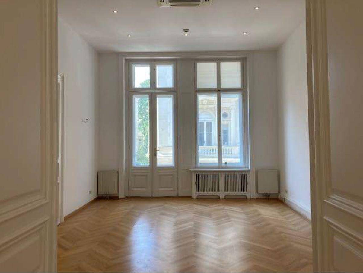 Großzügiger Raum mit Fischgrätparkett, hohen Fenstertüren und integrierter Deckenbeleuchtung.