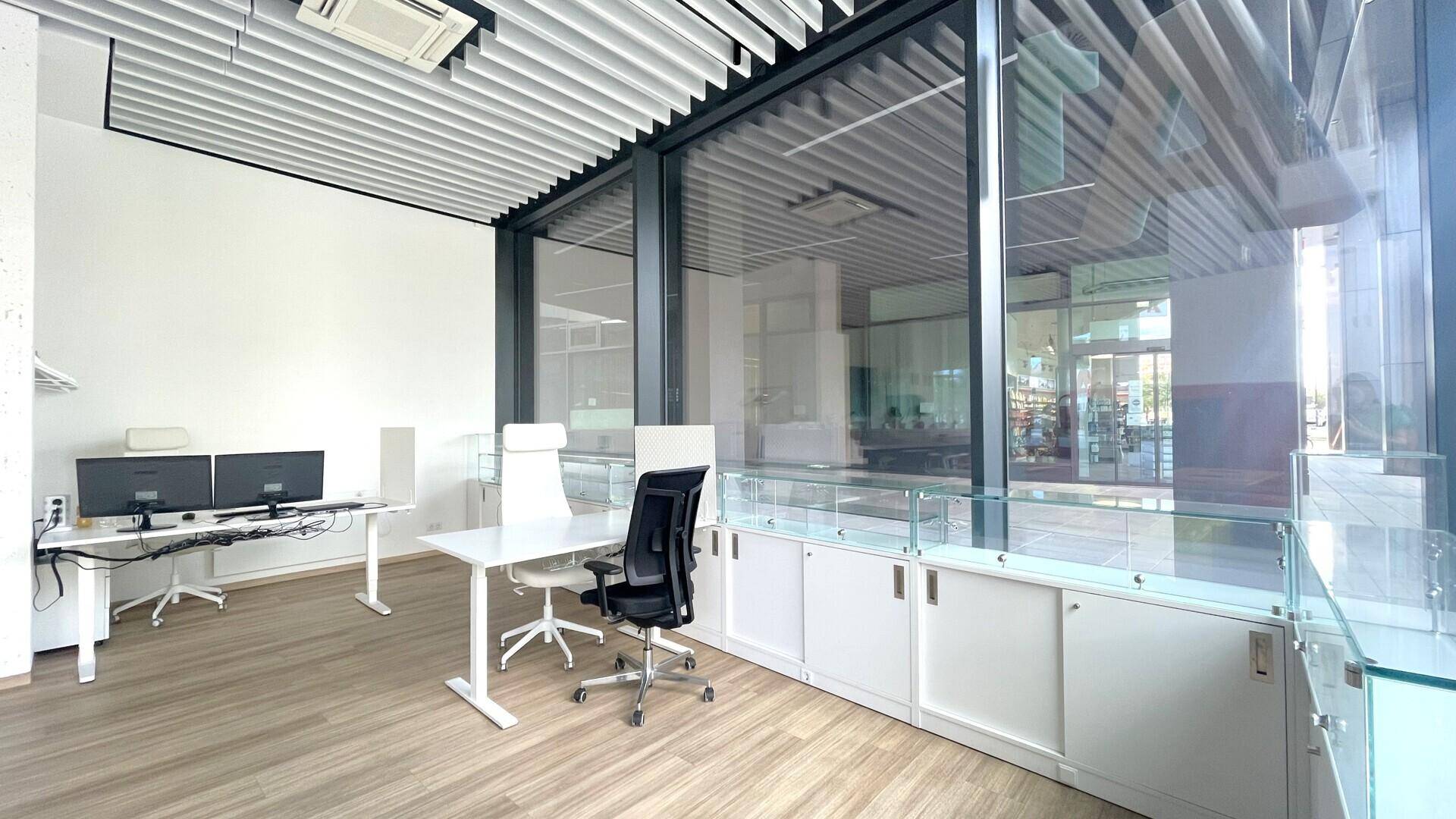 Heller Bürobereich mit großen Fensterfronten, modernen Schreibtischen und ergonomischen Stühlen für Mitarbeiter.