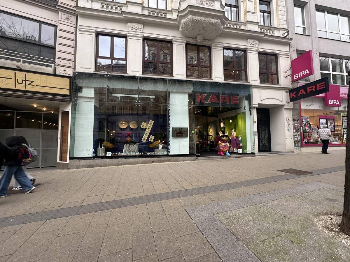 Geschäftsgebäude mit großen Schaufenstern und darüberliegenden Etagen an einer belebten Einkaufsstraße.