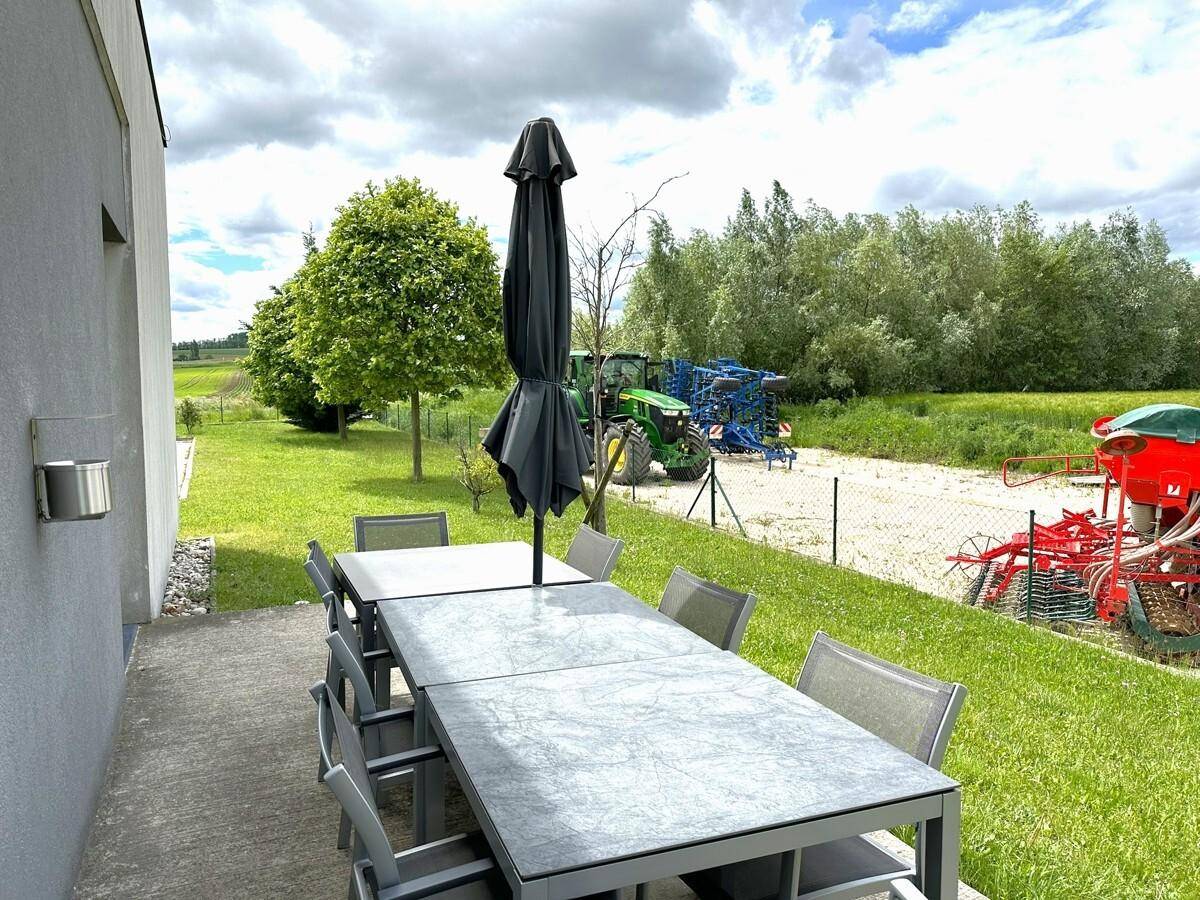 Gemütliche Terrasse mit Esstisch und Sonnenschirm, umgeben von grüner Landschaft und Feldern.