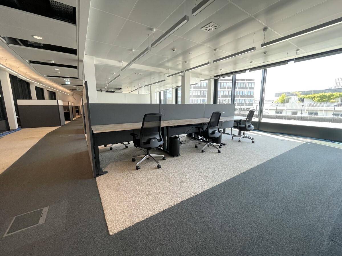 Heller und moderner Bürobereich mit ergonomischen Stühlen und Teppichboden in zwei Farbtönen.
