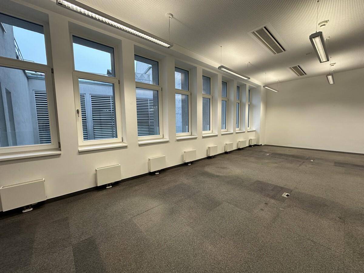 Heller, leerer Büroraum mit vielen Fenstern, Teppichboden und modernen Deckenleuchten, bereit zur Einrichtung.