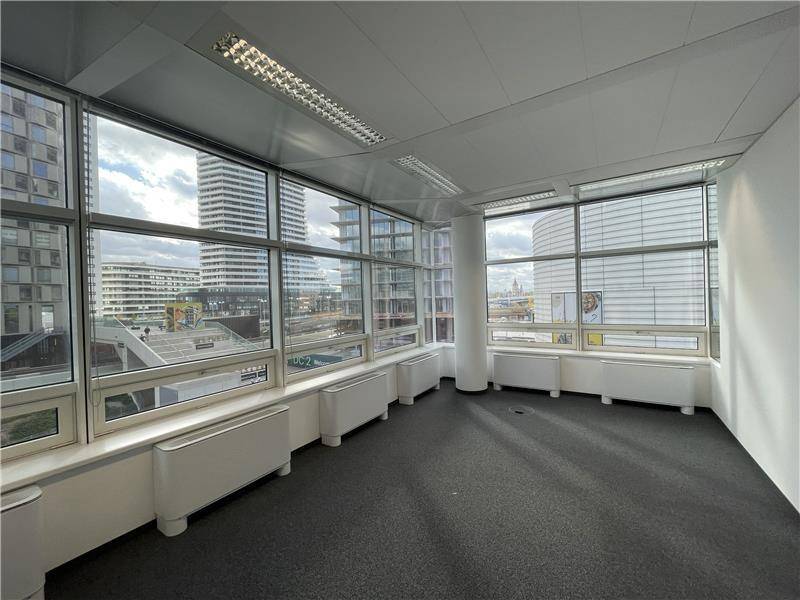 Großes, helles Büro mit Teppichboden und einer breiten Fensterfront, die einen weiten Blick auf die Stadt bietet.
