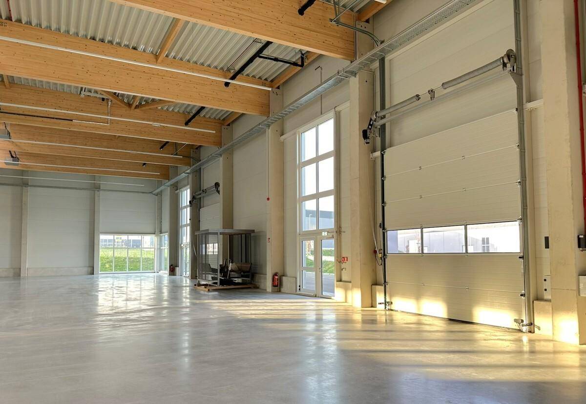 Geräumige Lagerhalle mit hohen Decken, Holzbalken und großen Fenstern, durchflutet von Sonnenlicht.