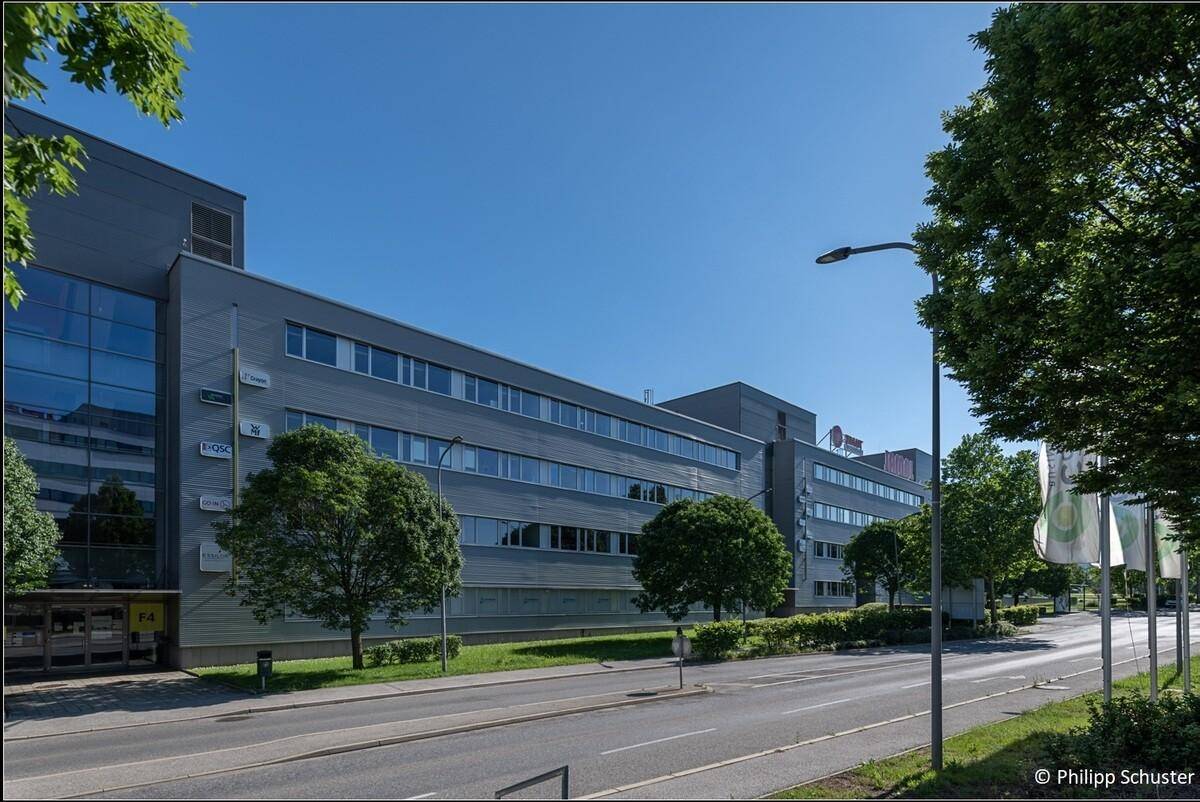 Moderne Bürogebäude mit großen Fenstern und gepflegter Grünfläche entlang einer sonnigen Straße.