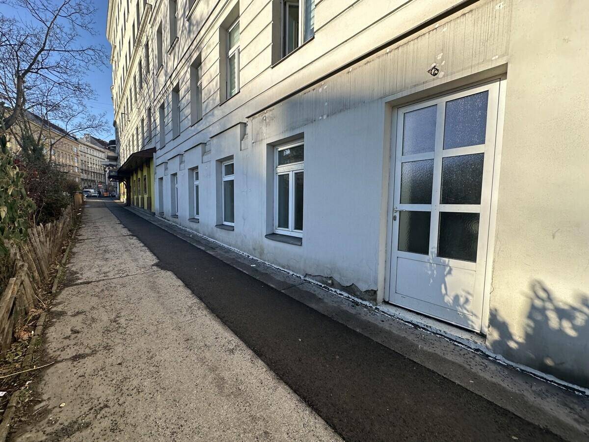 Seitenansicht des Gebäudes mit einer Reihe von Fenstern und einem Eingang auf Straßenniveau.