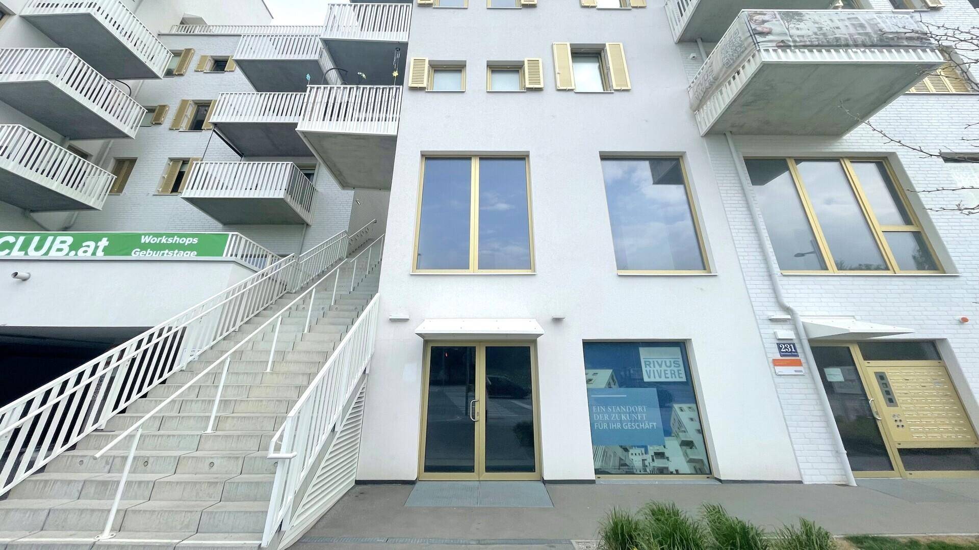 Ansicht der modernen Gebäudefassade mit zahlreichen Balkonen und großen Fenstern im Erdgeschoss.