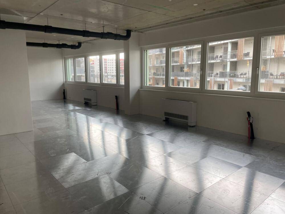 Heller Gewerberaum mit Fliesenboden, großen Fenstern und sichtbaren Deckeninstallationen, bereit zur Gestaltung.