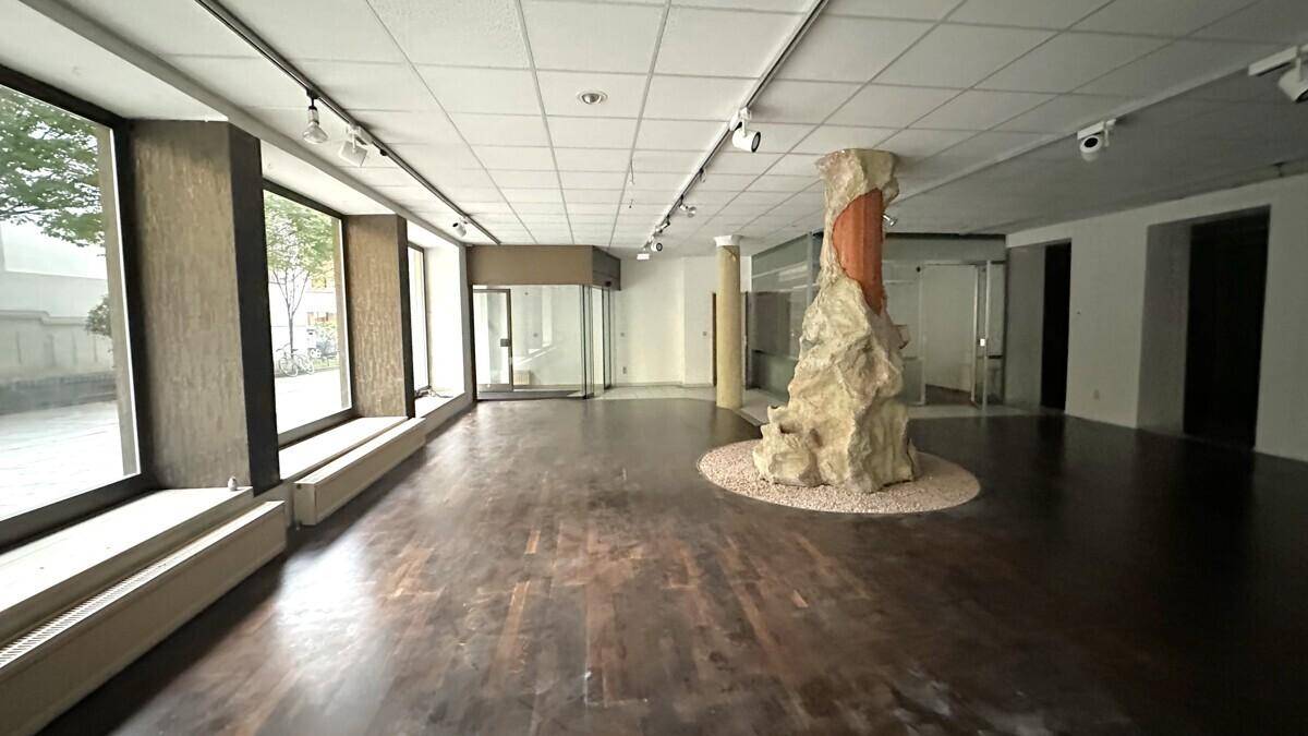 Großer Verkaufsraum mit dunklem Holzboden, einer markanten dekorativen Säule in der Mitte und viel Tageslicht.