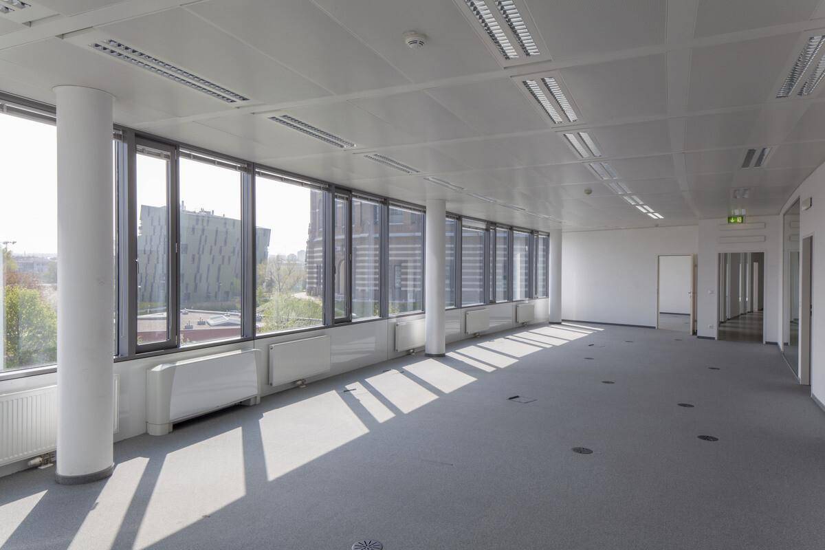 Heller, leerer Büroraum mit großen Fenstern, die eine weite Aussicht bieten, und einem modernen Teppichboden.