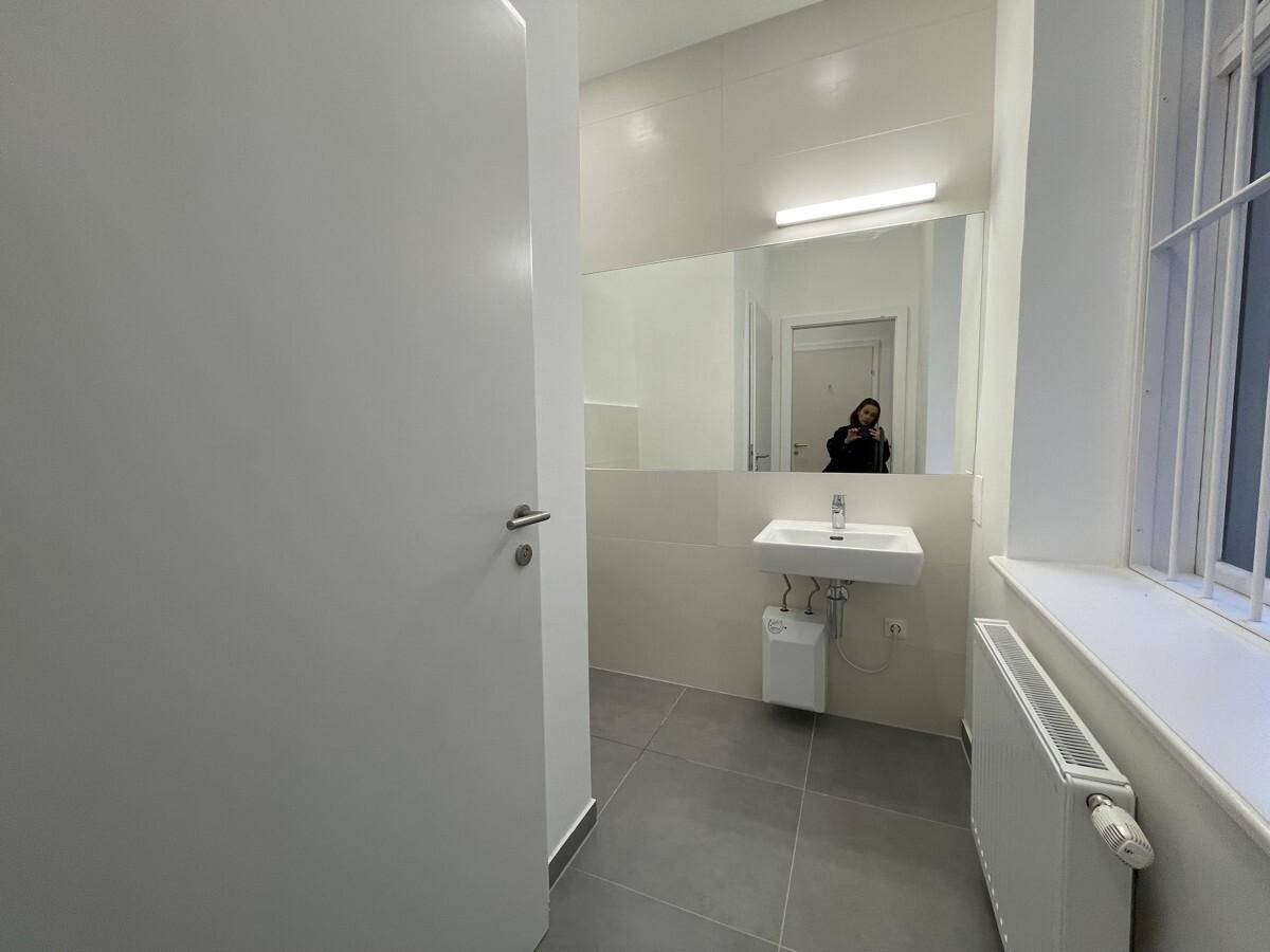 Modernes Badezimmer mit Waschbecken, großem Spiegel und Fenster, ausgestattet mit grauen Fliesen.