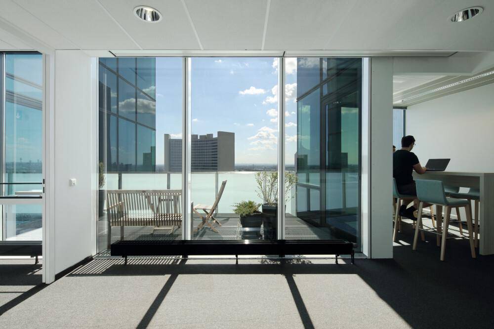 Heller Büroraum mit Zugang zu einer Terrasse, modernen Möbeln und weitem Blick über die Stadt.