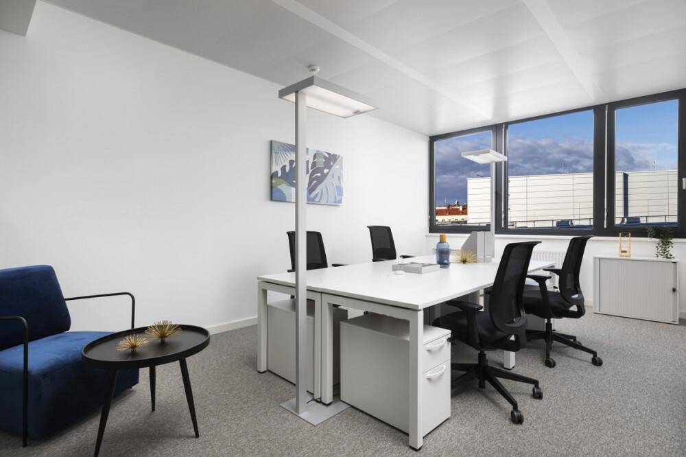 Modernes Büro mit weißem Schreibtisch, ergonomischen Stühlen und großen Fenstern, die viel Tageslicht hereinlassen.