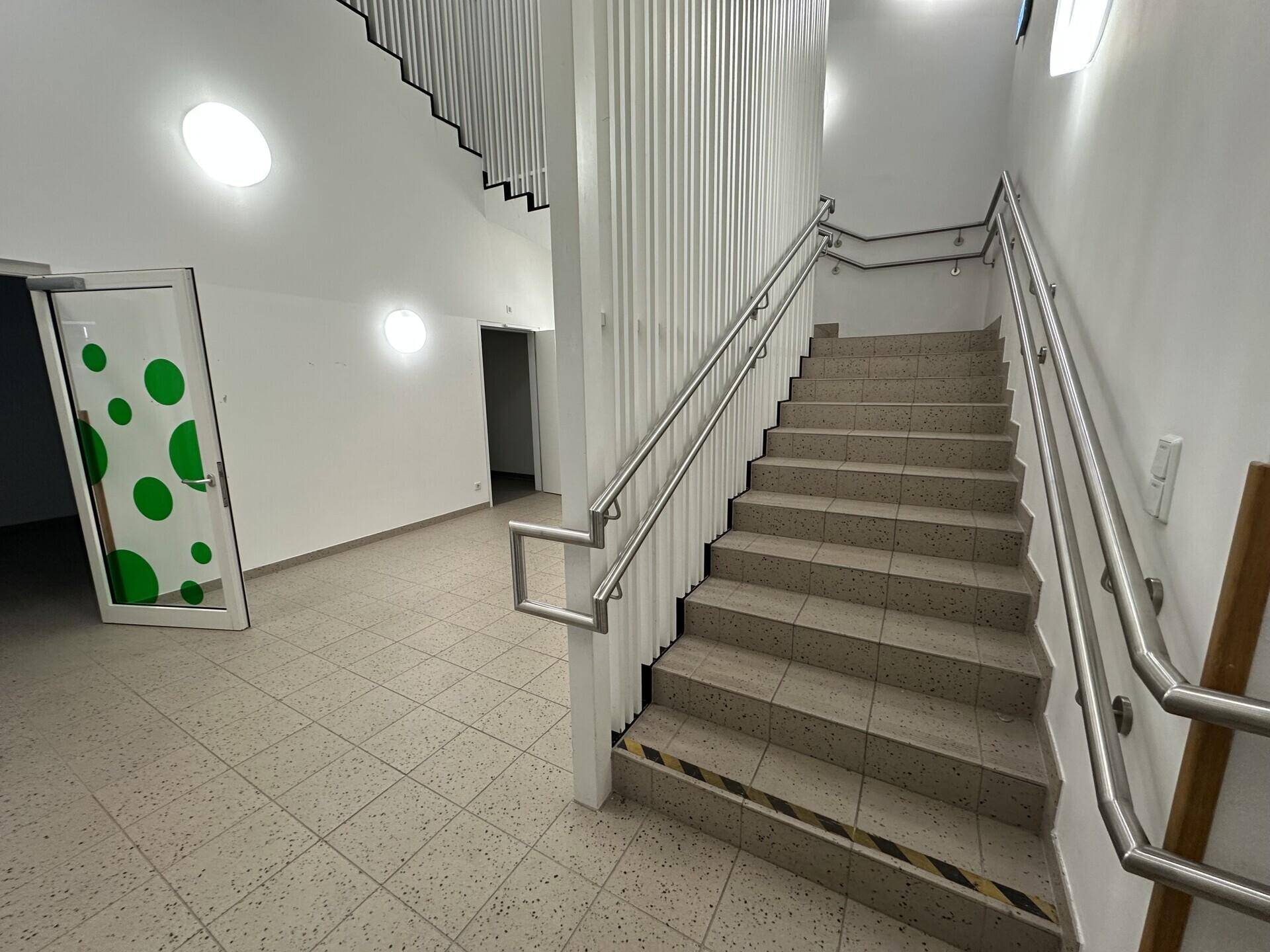 Helles Treppenhaus mit Fliesenboden und Metallgeländer, das zu den oberen Etagen führt.