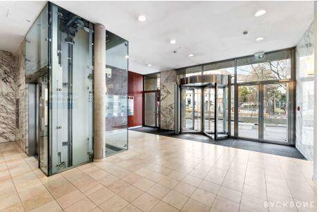 Moderne und helle Lobby mit Glasaufzügen, Marmorverkleidung und einer Drehtür zum Eingang.