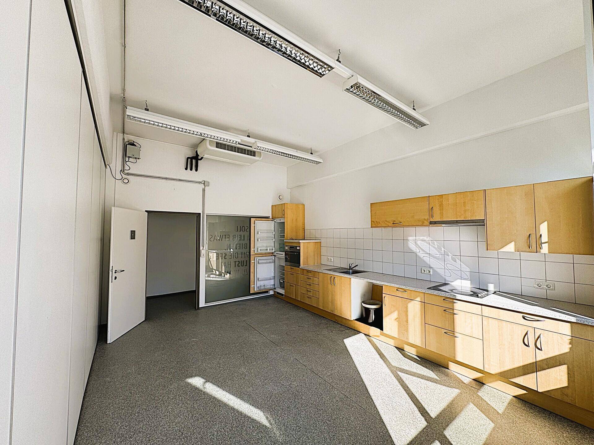 Funktionale Büroküche mit Holzschränken, Spüle und Kühlschrank, ideal für Mitarbeiter.