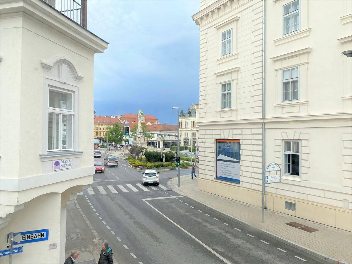 Blick aus dem Fenster auf eine belebte Straßenkreuzung mit Gebäuden und Fahrzeugen.