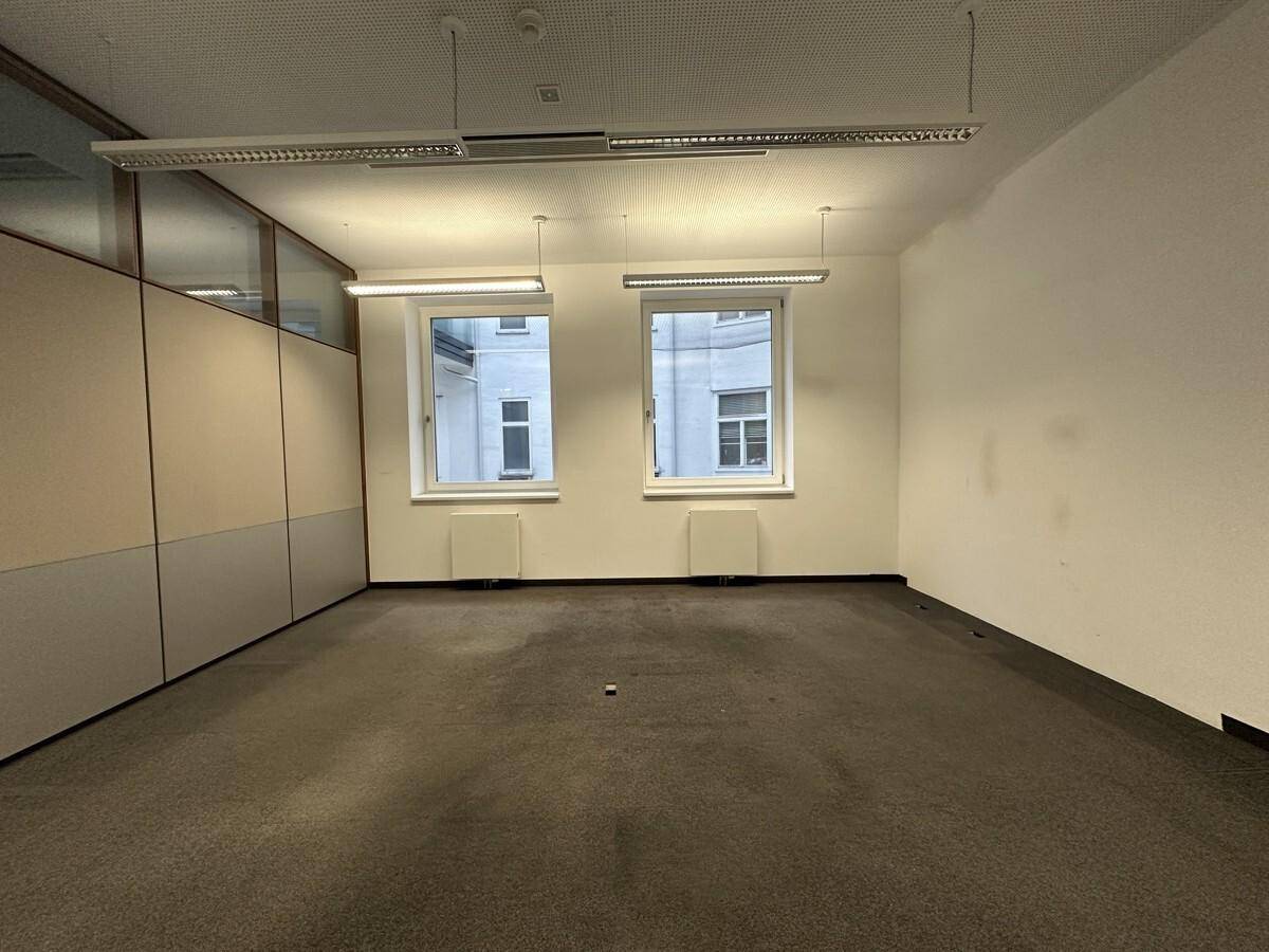 Leerer Büroraum mit Teppichboden, zwei Fenstern und integrierten Schränken, bereit zur individuellen Gestaltung.