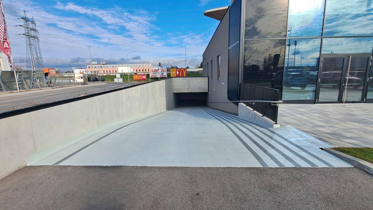Zufahrt zur Tiefgarage des Gebäudes mit moderner Architektur und angrenzender Treppe.