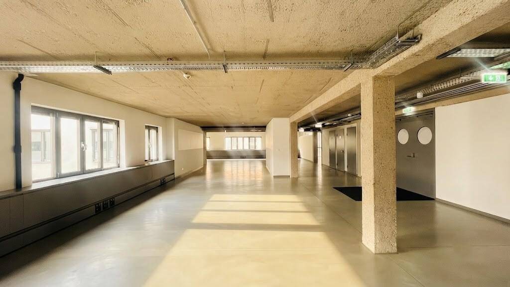Großer, offener Büroraum mit Betonboden und unverputzter Decke, der viel natürliches Licht durch die Fenster erhält.