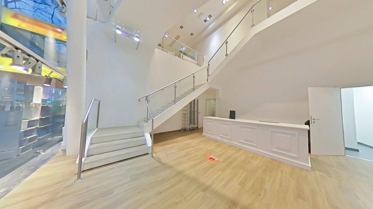 Heller und offener Verkaufsraum mit Holzboden, moderner Rezeption und Treppe zum Obergeschoss.