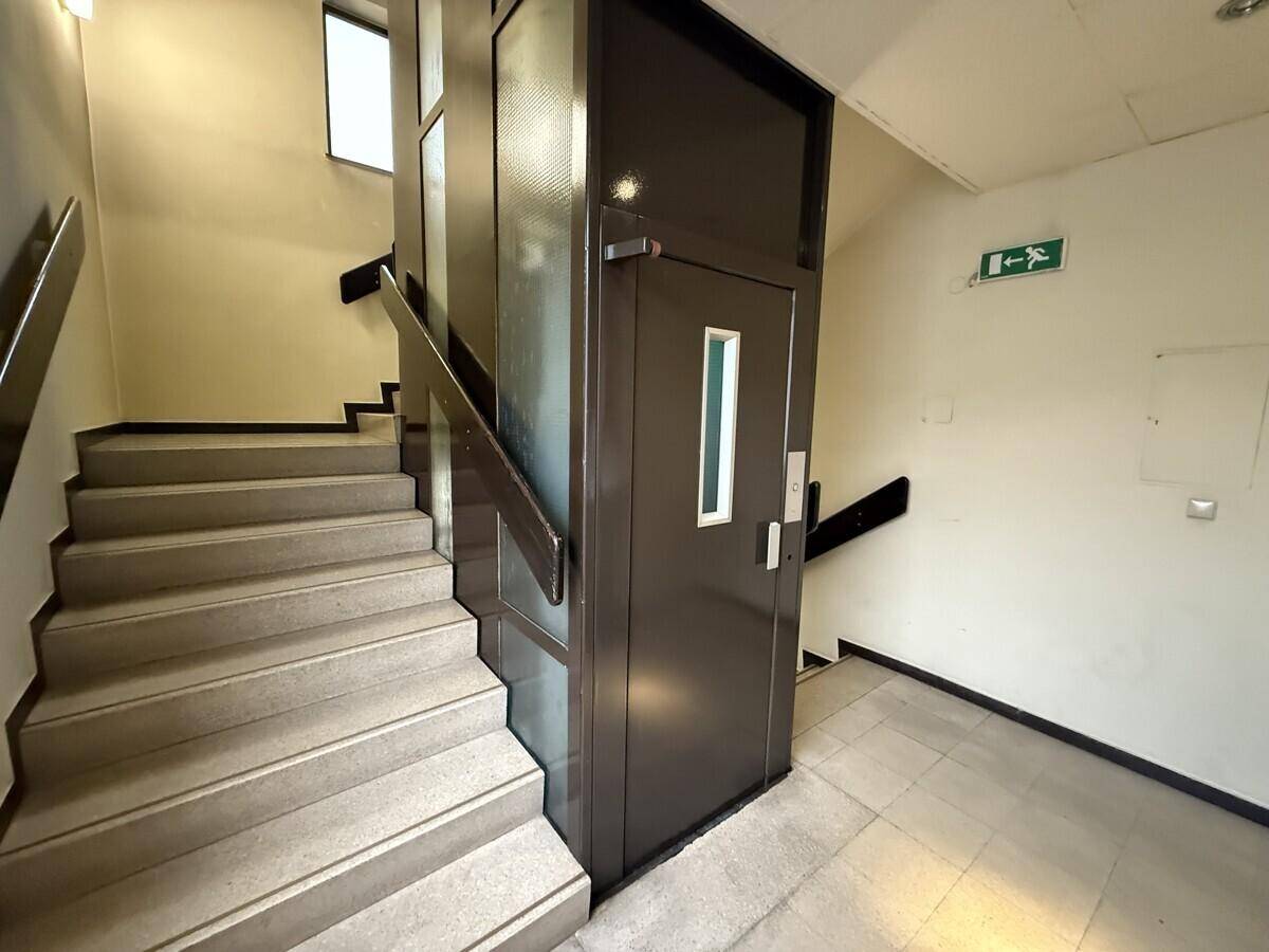 Treppenhaus mit Steinstufen und einem modernen Aufzug, der die verschiedenen Etagen verbindet.