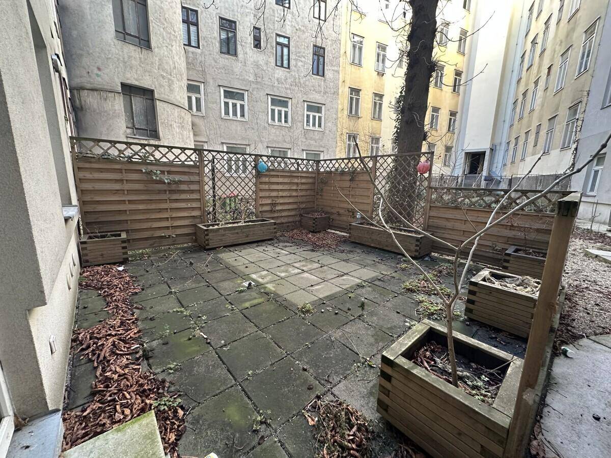 Innenhof mit gepflastertem Boden, Holzzäunen und einem Baum, der von Gebäuden umgeben ist.