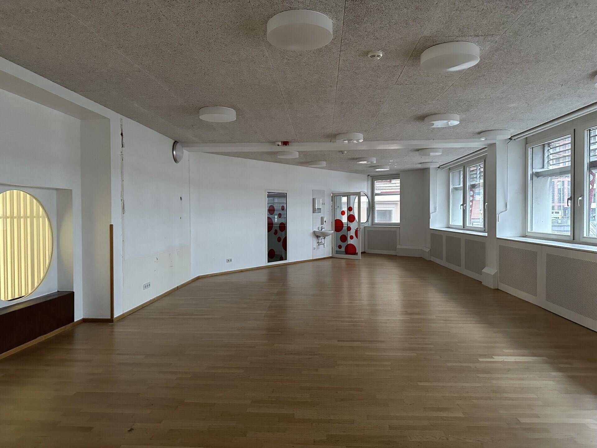 Geräumiger, heller Raum mit Holzboden und vielen Fenstern, geeignet für verschiedene Nutzungen.