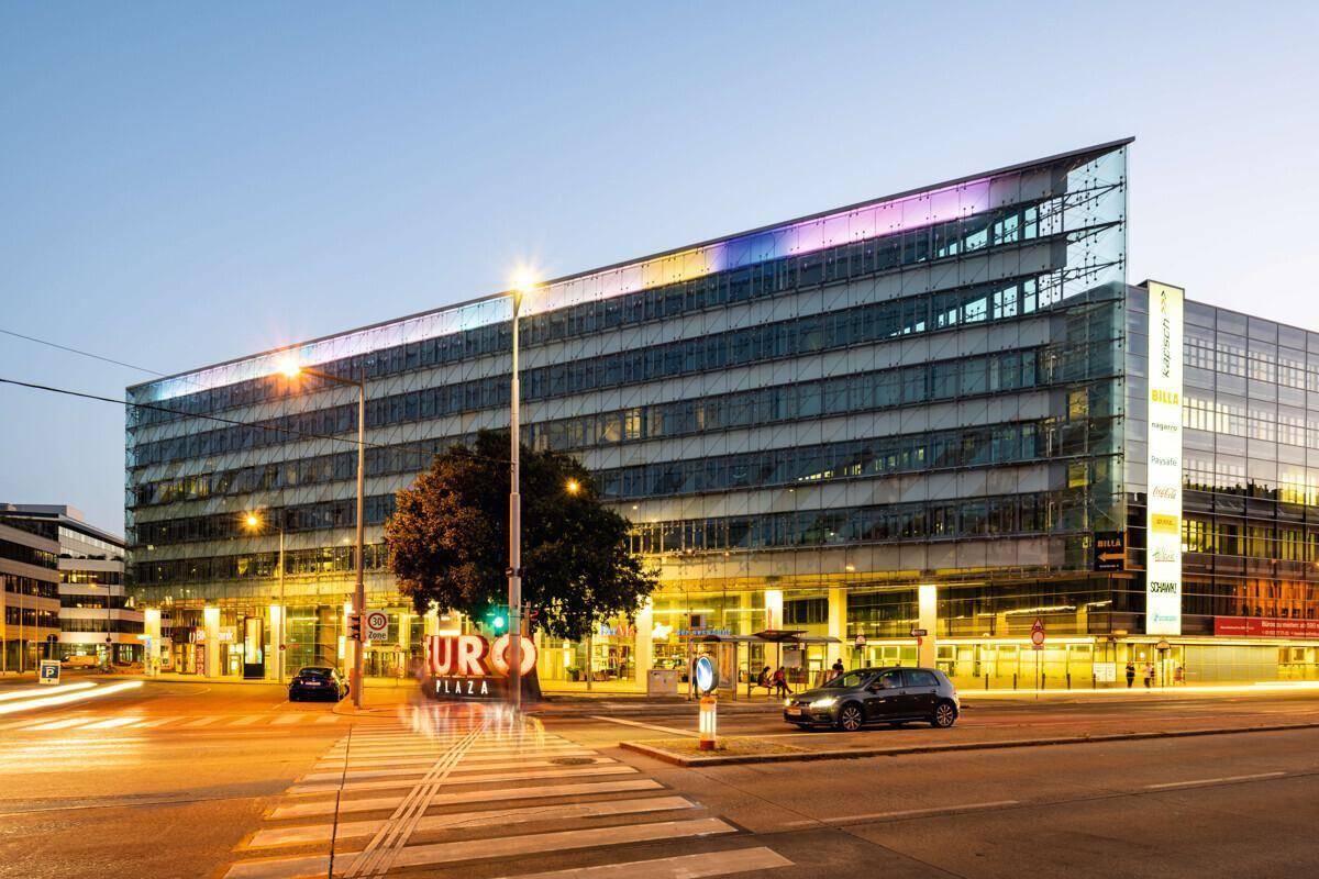 Modernes Bürogebäude mit farbiger Beleuchtung und beleuchtetem "EURO PLAZA" Schriftzug bei Dämmerung.