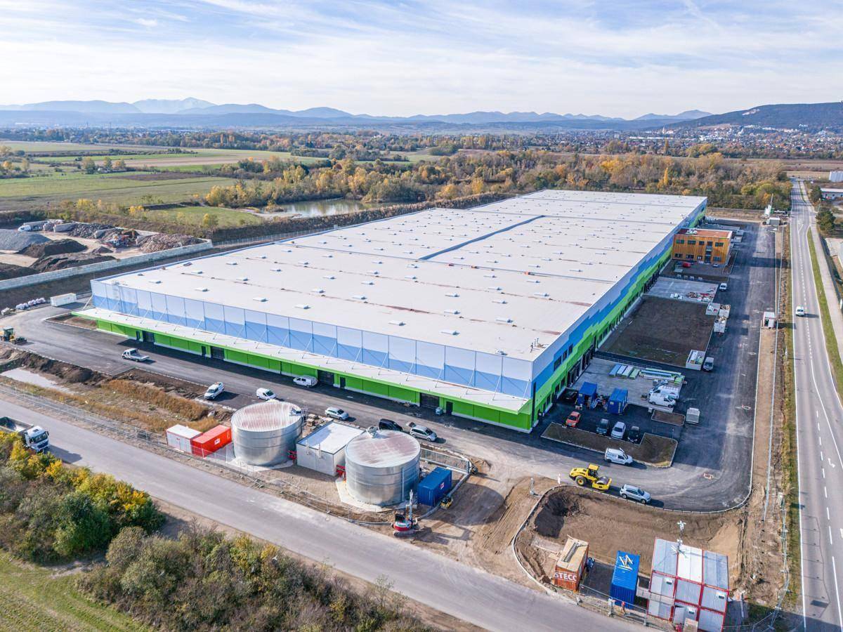 Luftaufnahme eines großen Logistikzentrums mit Laderampen und angrenzenden Straßen in ländlicher Umgebung.