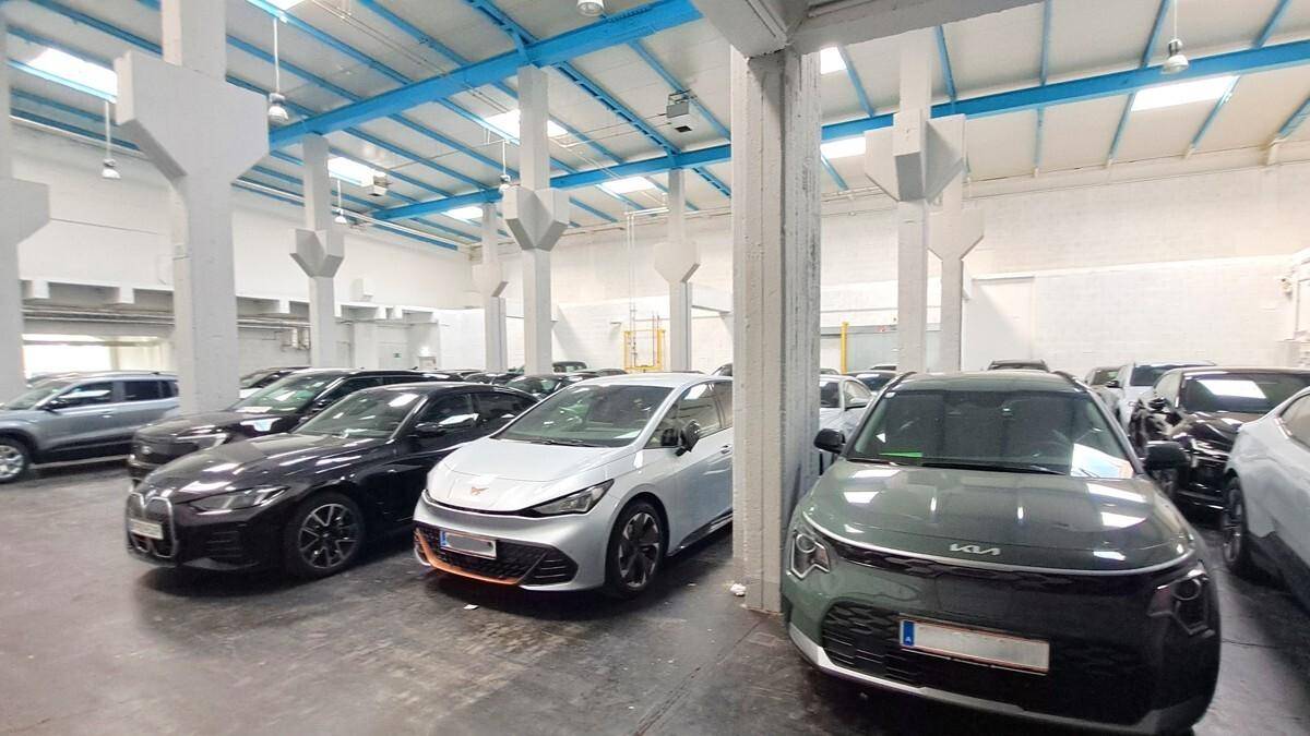 Große Halle mit vielen geparkten Autos, hohen Decken und Oberlichtern, die Tageslicht hereinlassen.
