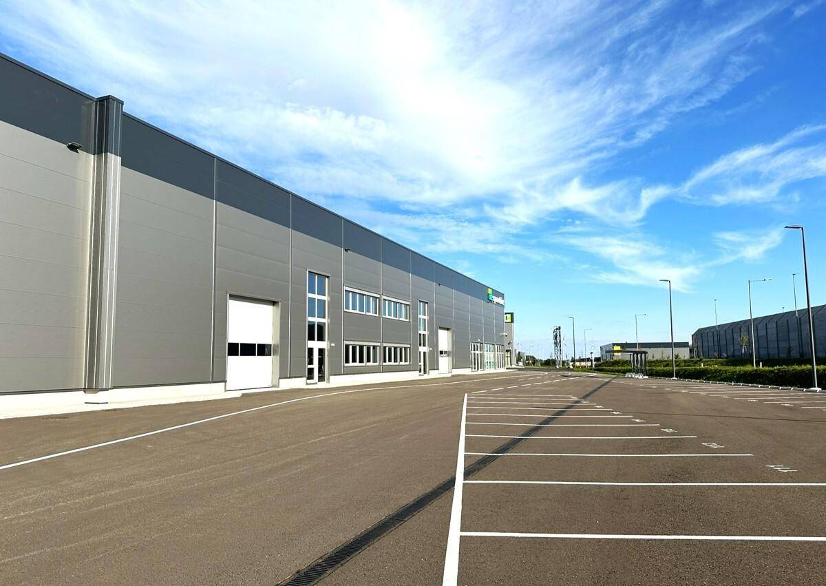 Lange Fassade eines modernen Gewerbegebäudes mit vielen Parkplätzen unter weitem Himmel.