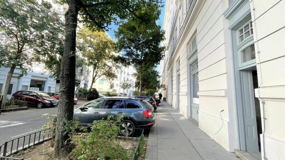 Ruhige Straße mit parkenden Autos, Bäumen und der Fassade eines historischen Gebäudes.