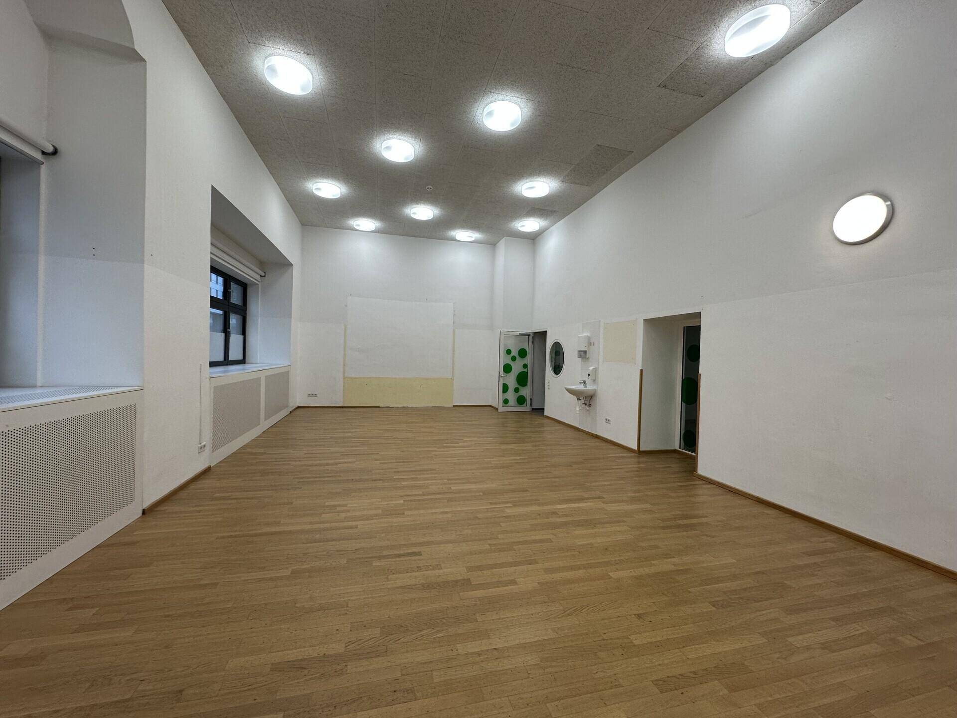 Großer, leerer Raum mit Holzboden, hohen Decken und mehreren Fenstern, ideal für flexible Nutzung.