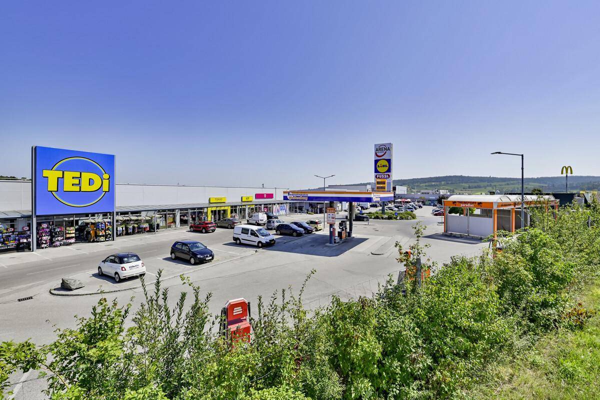Übersicht über ein Gewerbegebiet mit Geschäften, Tankstelle und Autowaschanlage unter blauem Himmel.