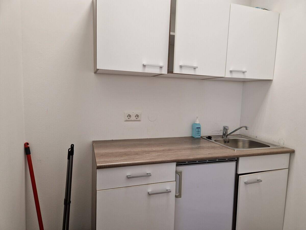 Kleine Küchenzeile mit weißen Schränken, Arbeitsplatte in Holzoptik, Spüle und Unterbaukühlschrank.